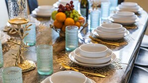 Een eettafel gedekt met witte borden, kommen en groen glaswerk, met gouden bestek en decoratieve objecten.