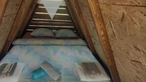 Un dormitorio abuhardillado con estructura de madera, una cama, almohadas y una mesita.