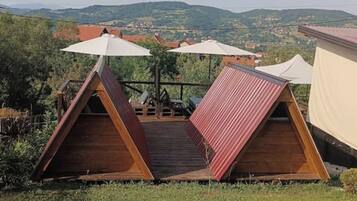 Two wooden A-frame tents with white canopies, set on a wooden deck with a view of a hilly landscape.