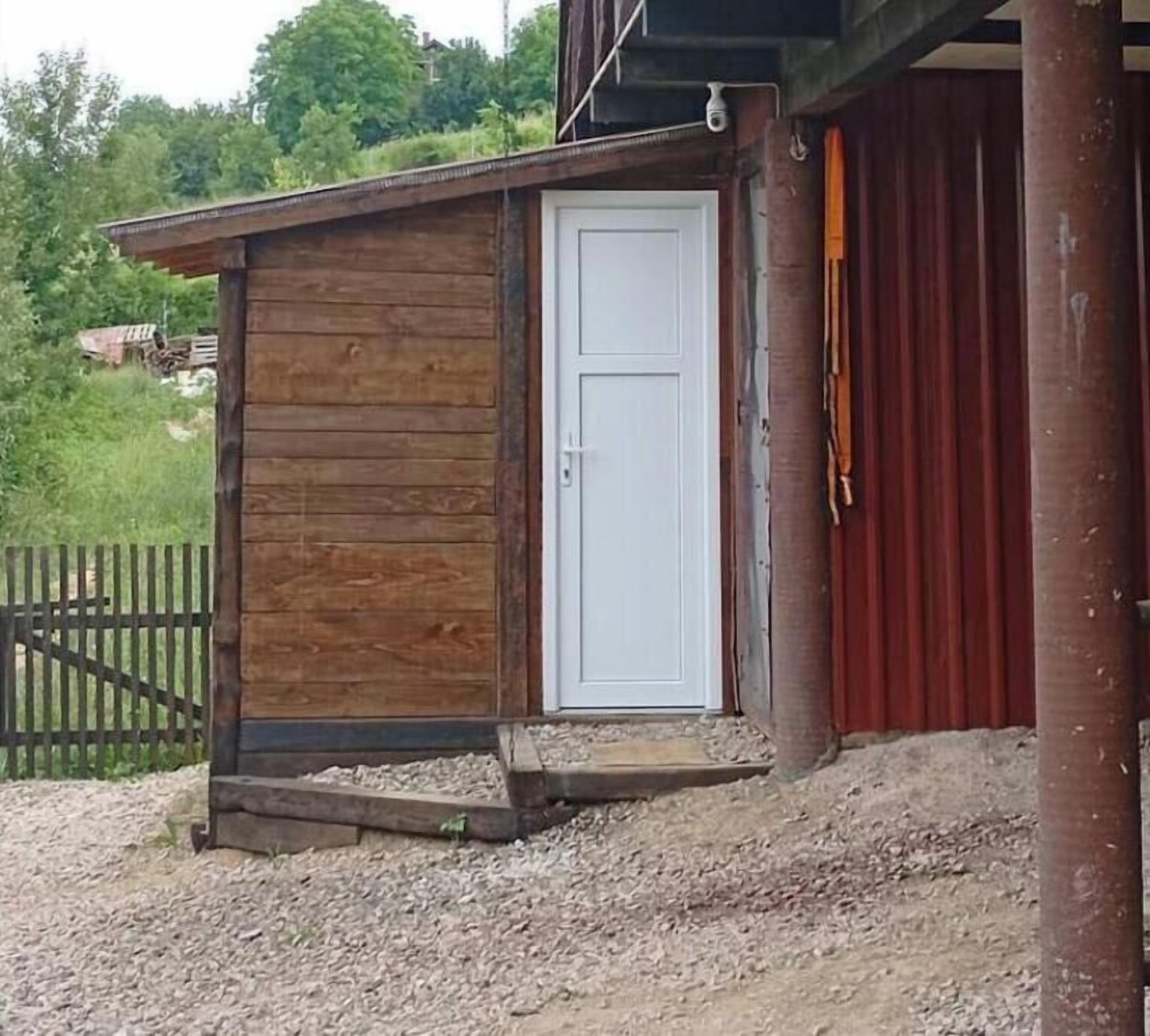 Une petite construction en bois avec une porte blanche, un sol recouvert de gravier et une clôture en bois en arrière-plan.