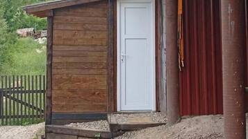 Une petite construction en bois avec une porte blanche, un sol recouvert de gravier et une clôture en bois en arrière-plan.