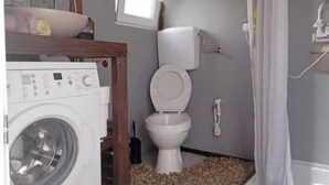 Un baño pequeño con lavadora, inodoro y zona de ducha.