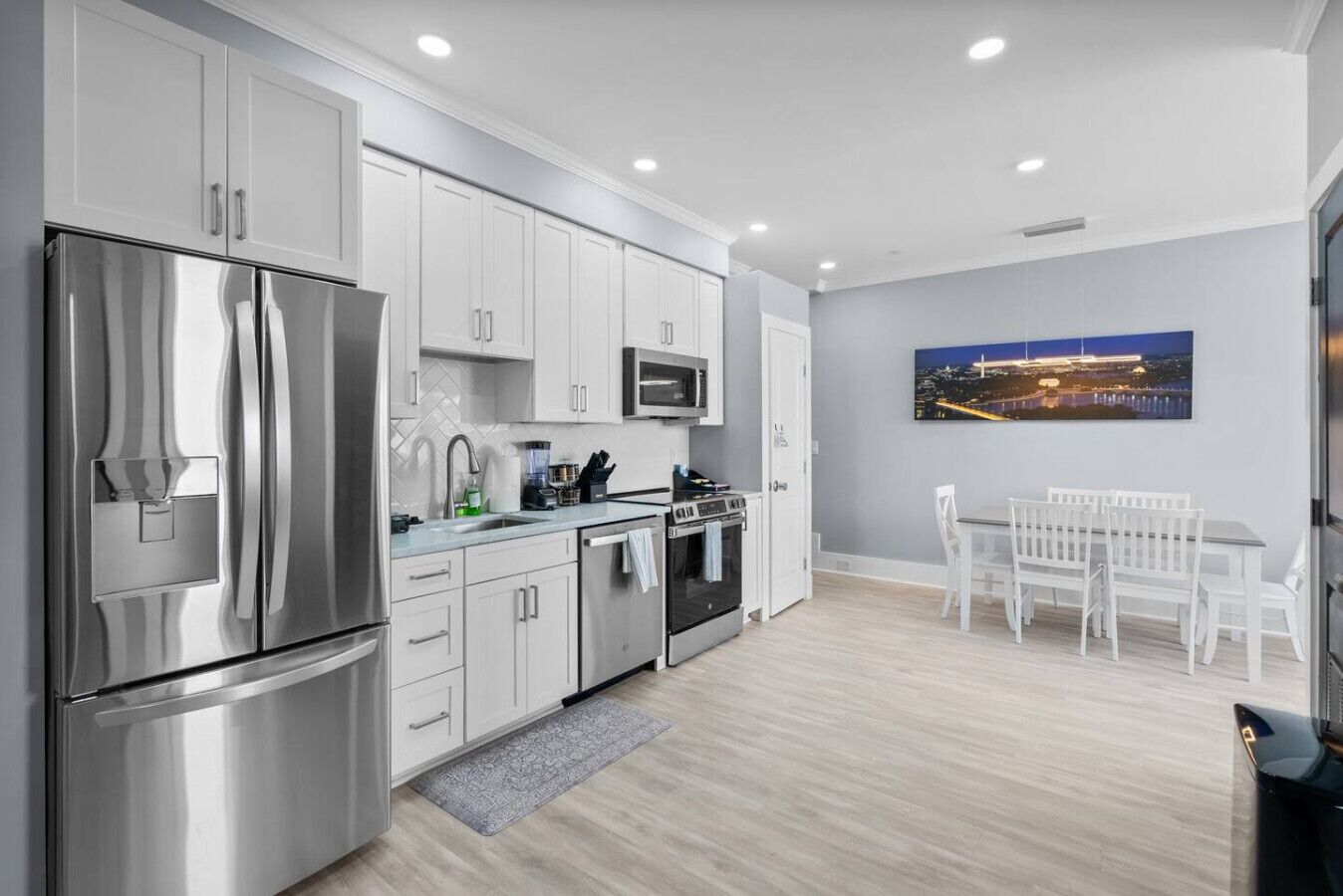 A modern kitchen with stainless steel appliances, white cabinetry, and a dining area with a table and chairs.