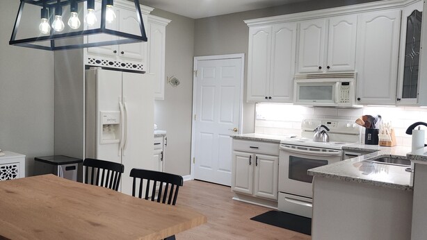 Een moderne keuken met witte kastjes, een houten eettafel en een zwart hanglamp.