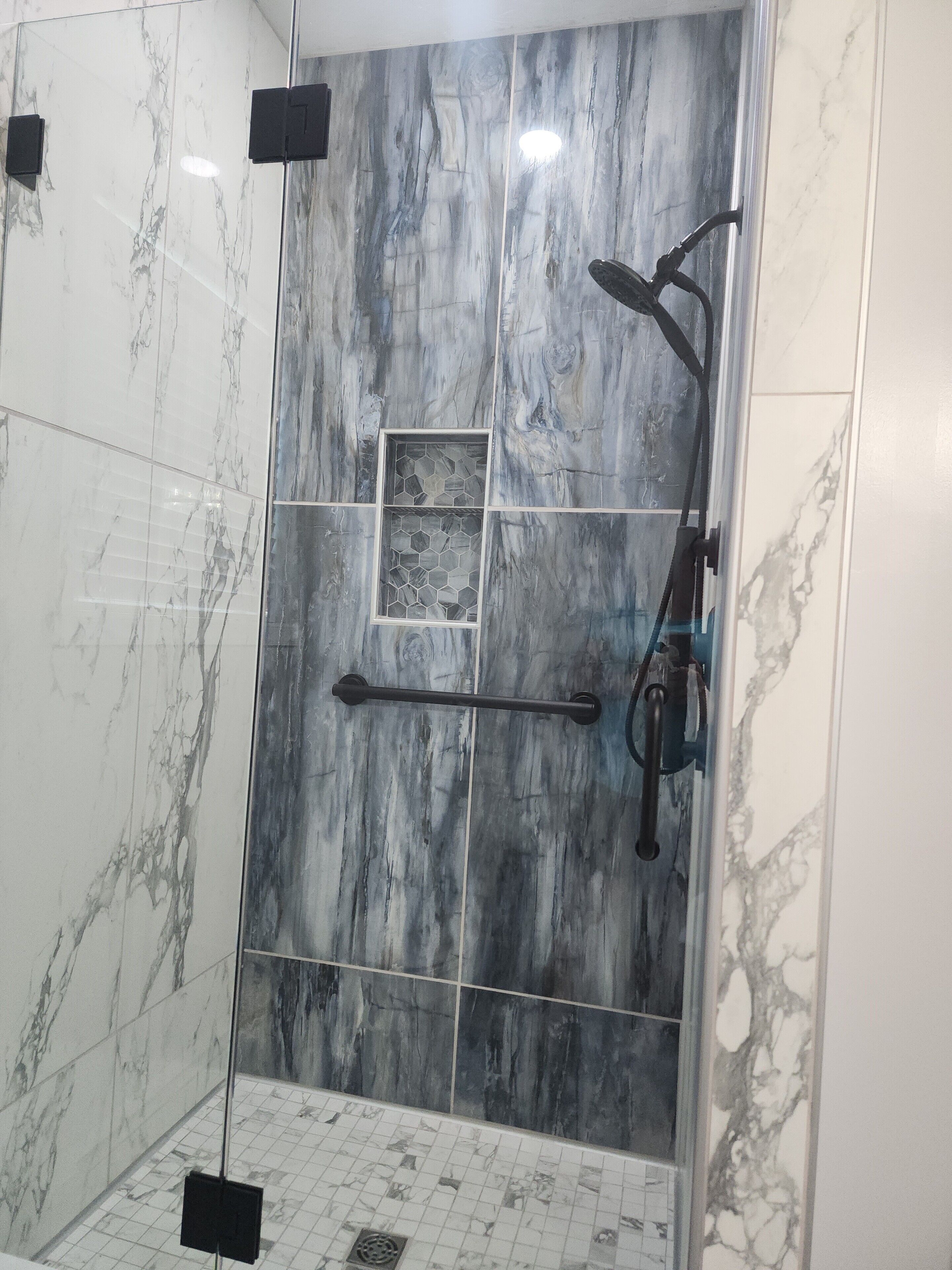 A modern shower with a glass door, marble tiles, and a rain showerhead.