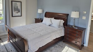 Een slaapkamer met een groot bed, twee nachtkastjes met lampen, een lijst met een afbeelding aan de muur en een raam met gordijnen.