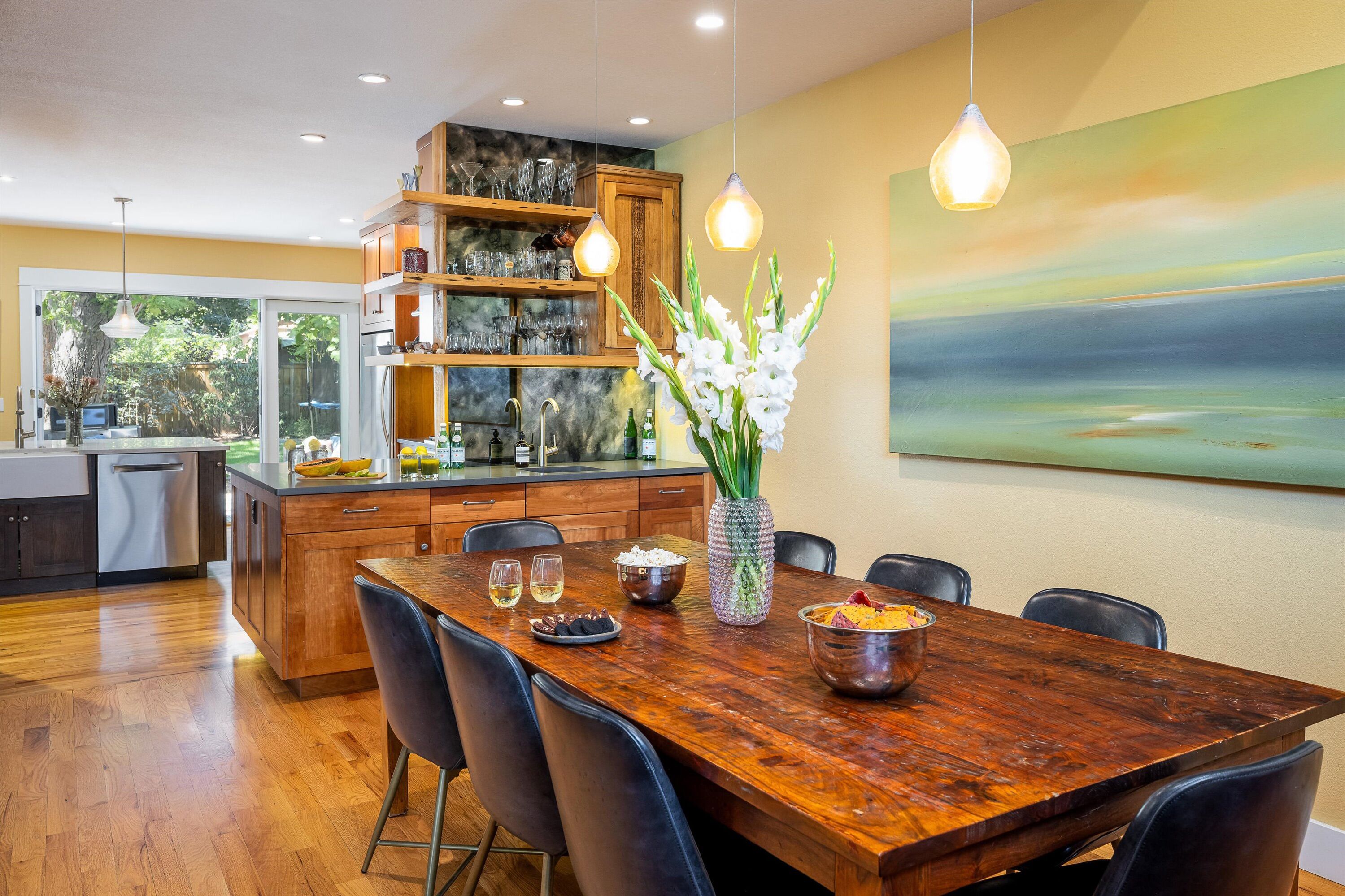 A modern kitchen with wooden cabinets, a dining table with chairs, and a large island with a sink.