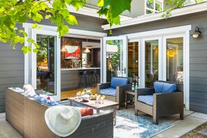 An outdoor patio with wicker furniture, a dining table, and a view into the house.