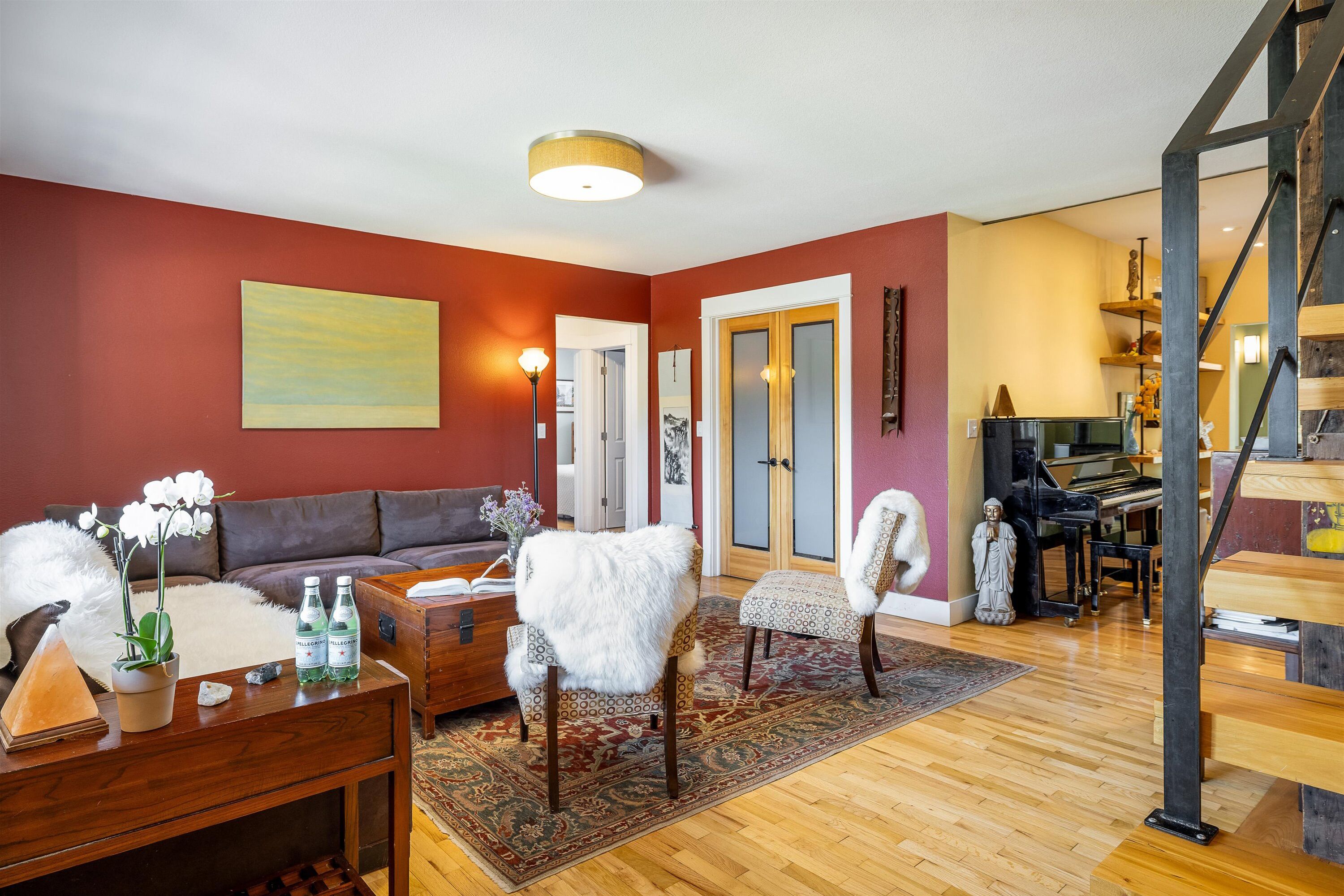 Een woonkamer met een bruine bank, twee witte stoelen, een houten salontafel en een rode accentmuur.