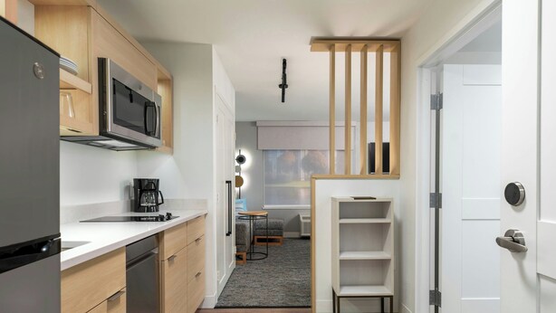 Una cocina moderna equipada con refrigerador, microondas y cafetera. Hay un pequeño comedor con una mesa y sillas, y una ventana con persianas.