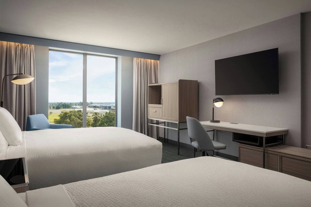 Ein Hotelzimmer mit zwei Betten, einem Schreibtisch, einem Sessel und Blick auf die Stadt.