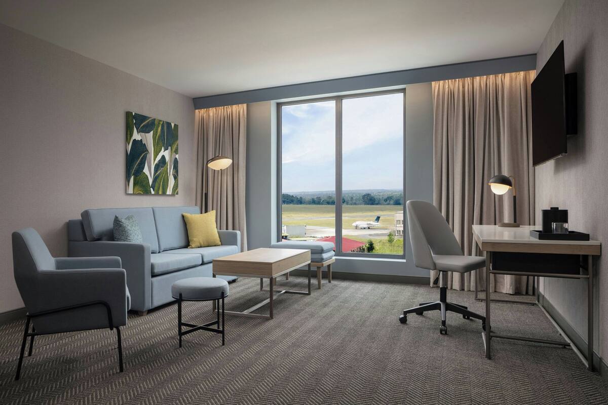 Ein modernes Hotelzimmer mit großem Fenster, einer Couch, einem Schreibtisch und einem Stuhl.