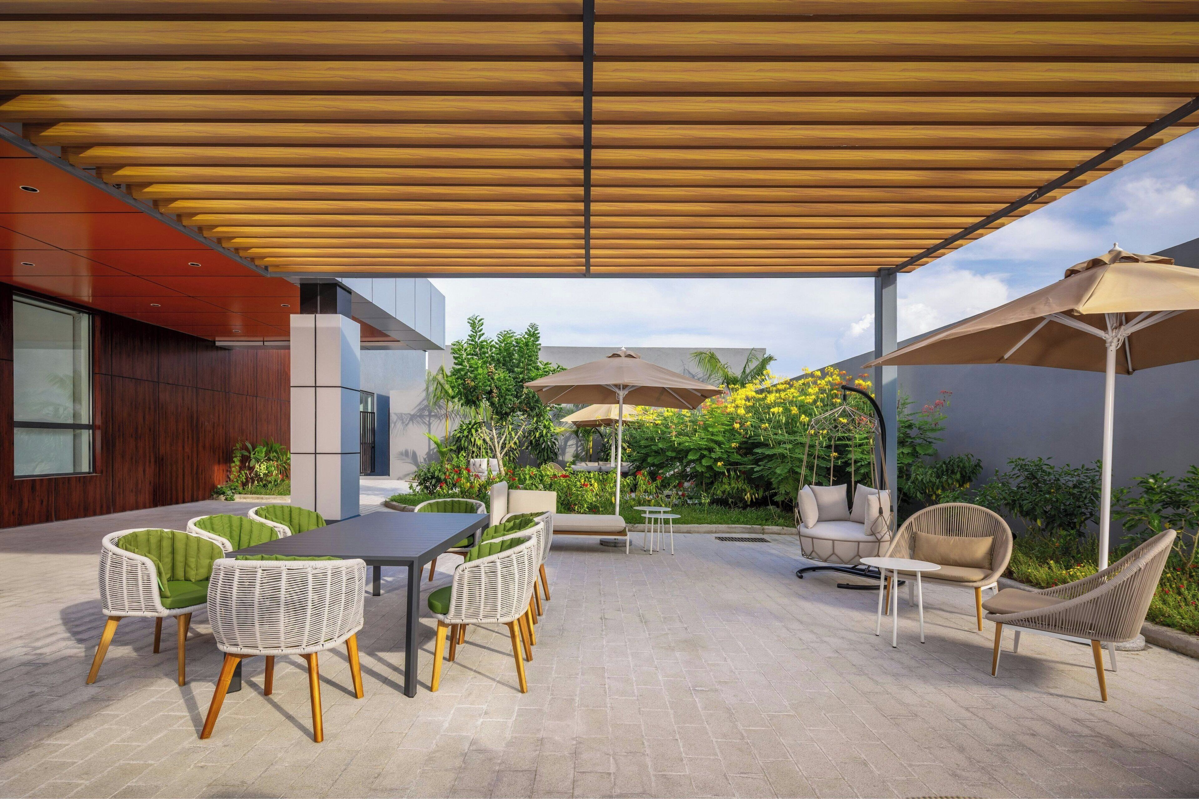 Un patio exterior con una pérgola de madera, muebles de mimbre y una mesa.