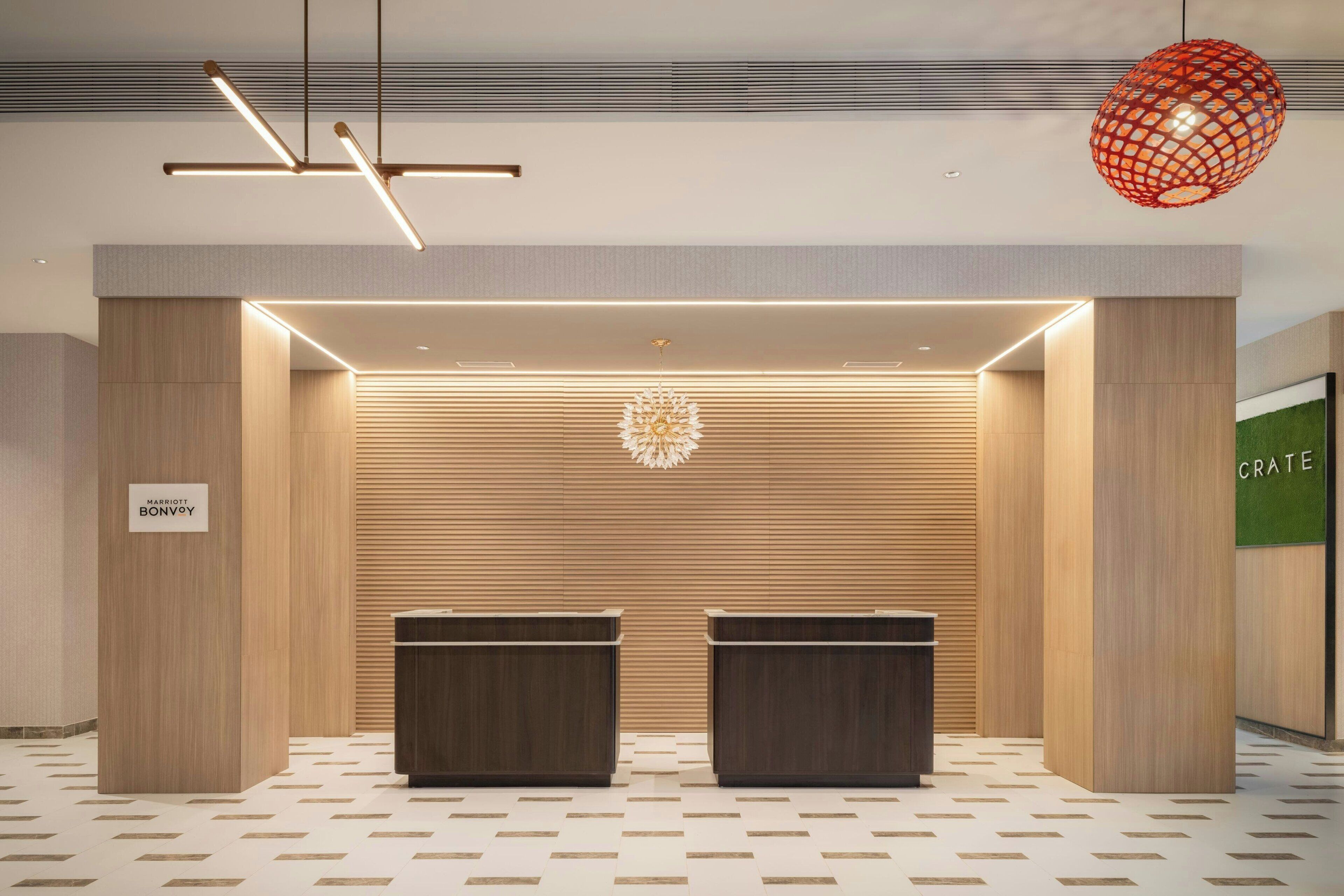Una moderna zona de recepción con dos mostradores de madera oscura, un suelo con estampado geométrico y una lámpara colgante esférica original.