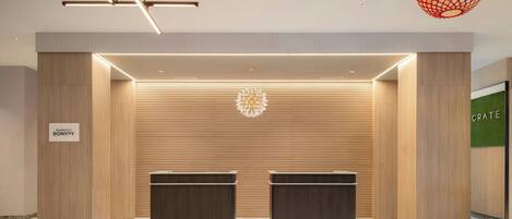 Una moderna zona de recepción con dos mostradores de madera oscura, un suelo con estampado geométrico y una lámpara colgante esférica original.