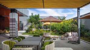 An outdoor patio area with a dining table, chairs, and a swing chair. - Courtyard Cheddi Jagan International Airport, Guyana (Timehri)