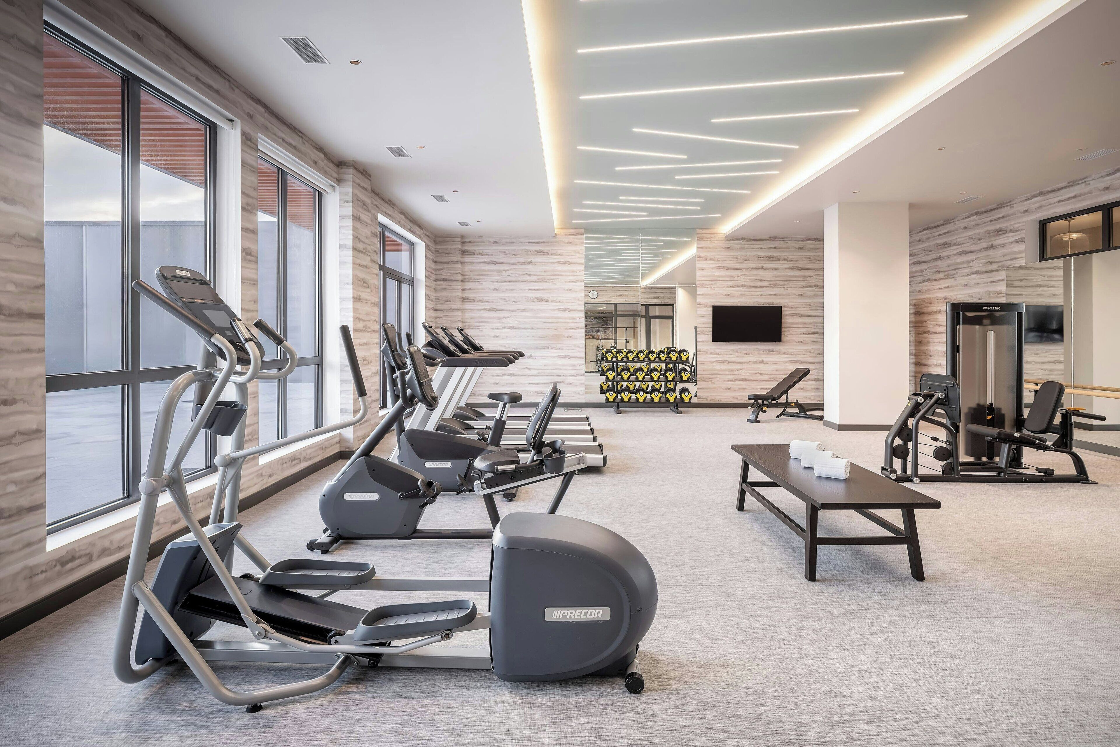 Une salle de sport moderne équipée de tapis de course, de vélos elliptiques et de matériel de musculation.
