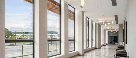 A spacious corridor with large windows, a tiled floor, and modern lighting fixtures.