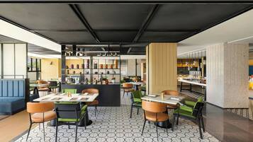 A modern restaurant interior with hexagonal patterned flooring, black and green upholstered chairs, and a central bar area with shelves of bottles and glasses.