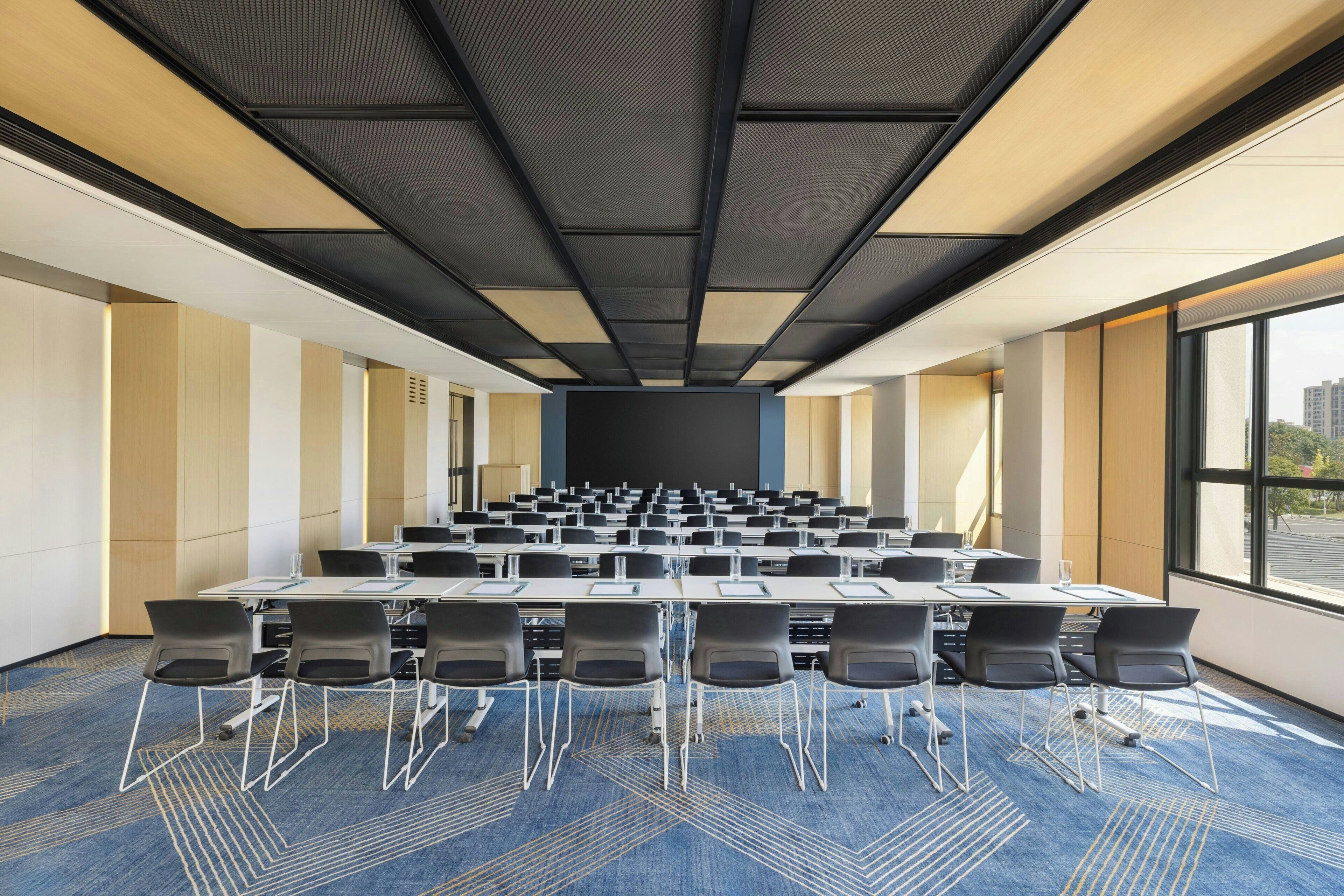 A conference room with a long table and chairs, large windows, and a high ceiling.