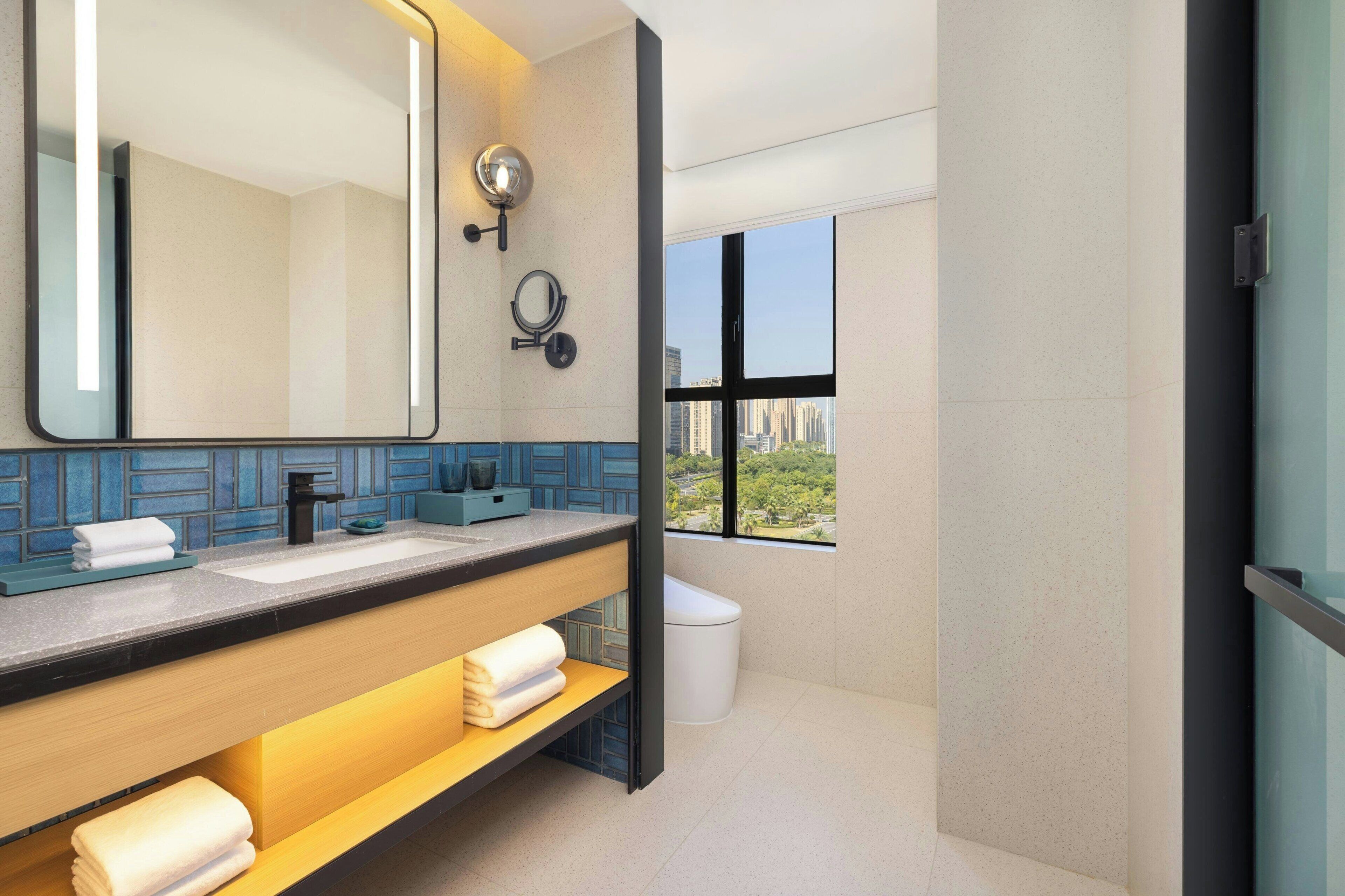 Un baño moderno con un espejo grande, lavamanos dobles y ventana con vista a la ciudad.