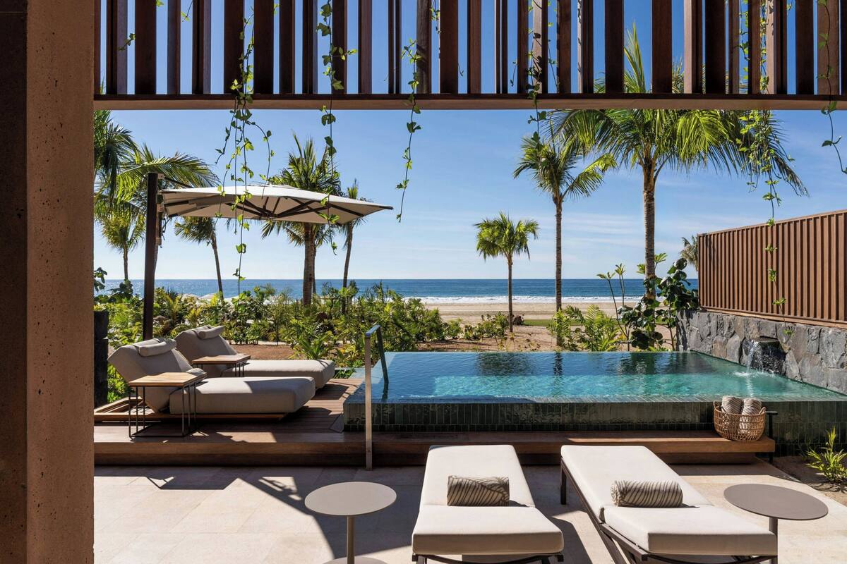 An infinity pool with a view of the beach, lounge chairs, and umbrellas.