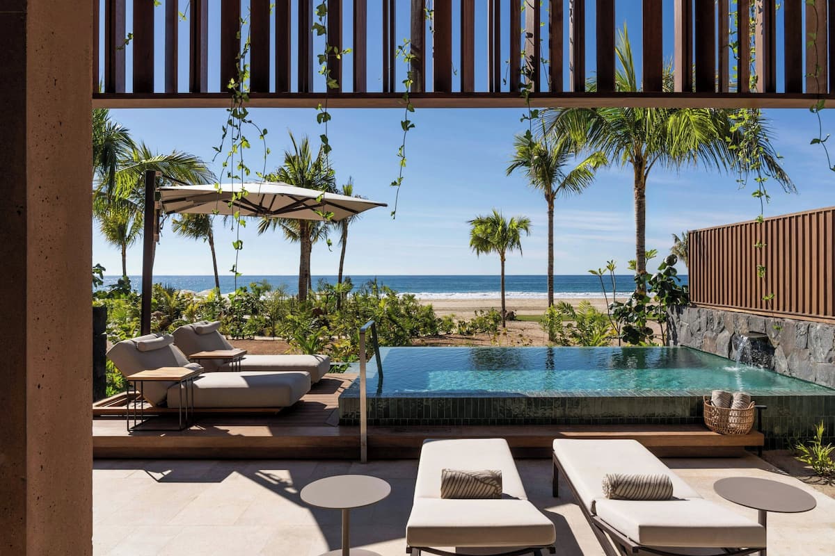 Une piscine à débordement offrant une vue sur la plage, ainsi que des chaises longues et des parasols.