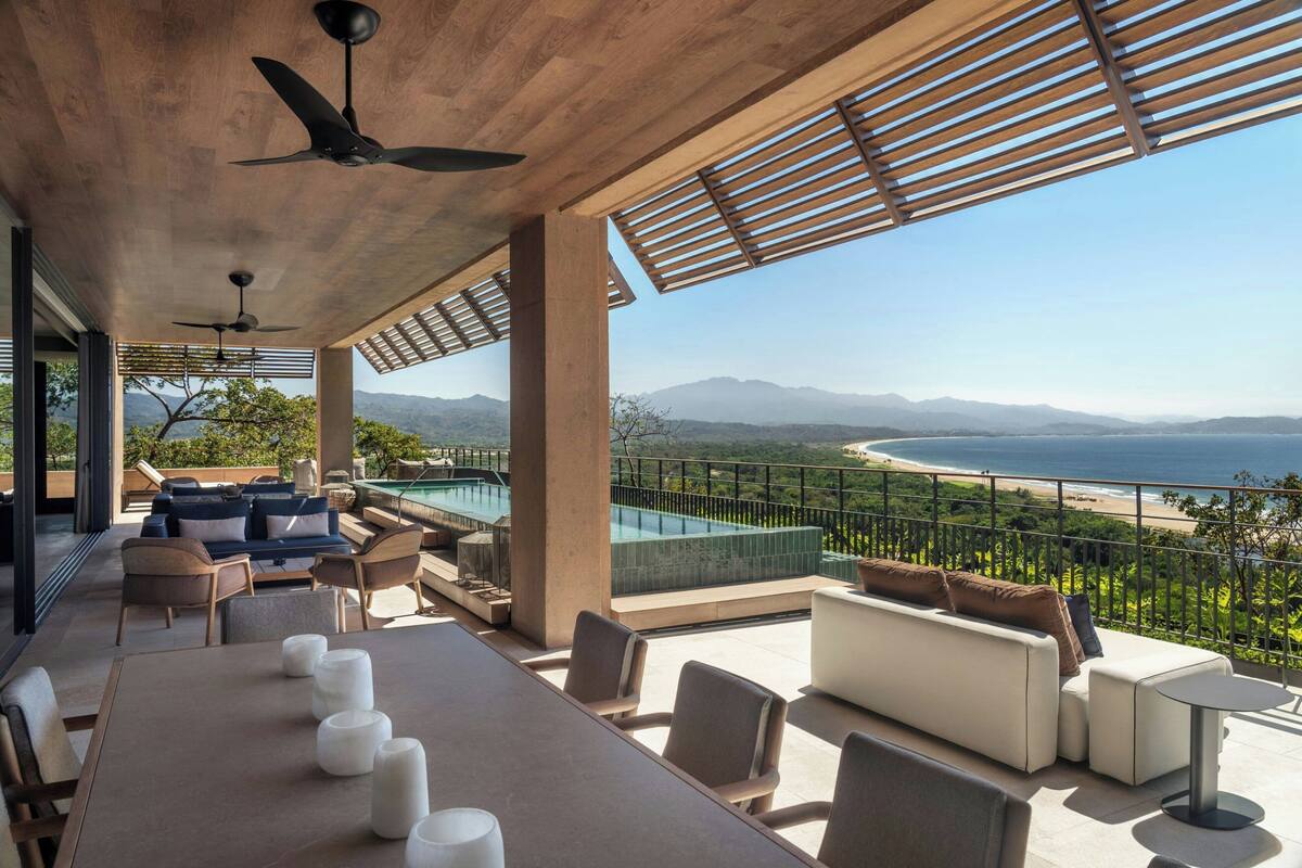 A modern outdoor lounge area with a pool, seating, and a view of the ocean and mountains.
