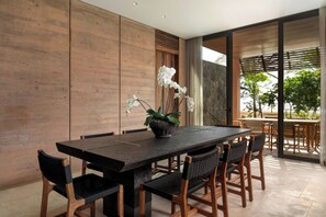 A modern dining area with a dark wooden table, black woven chairs, and a potted orchid plant.
