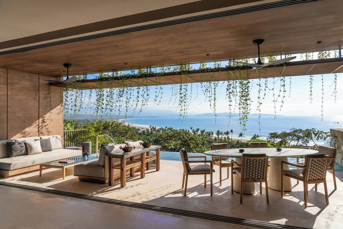 A modern outdoor living space with a sofa, dining table, and chairs, overlooking a scenic ocean view.
