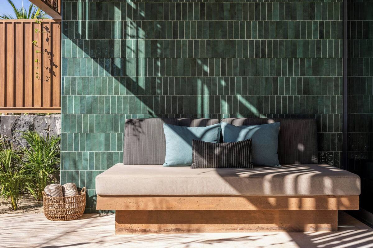 A bed with pillows, a woven basket, and a tiled wall.