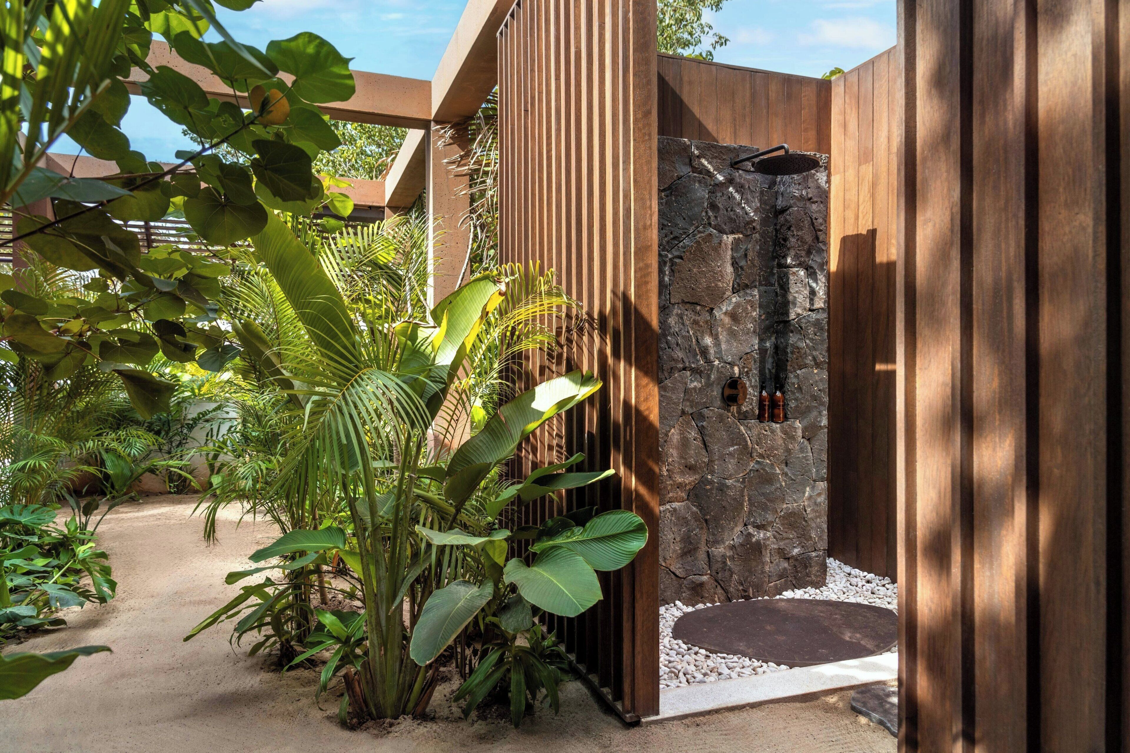 Un jardín tropical con muro de piedra, paneles de madera y diversas plantas.