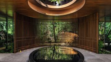 Un elemento acuático circular con techo de madera y vista a un bosque a través de una celosía de bambú.