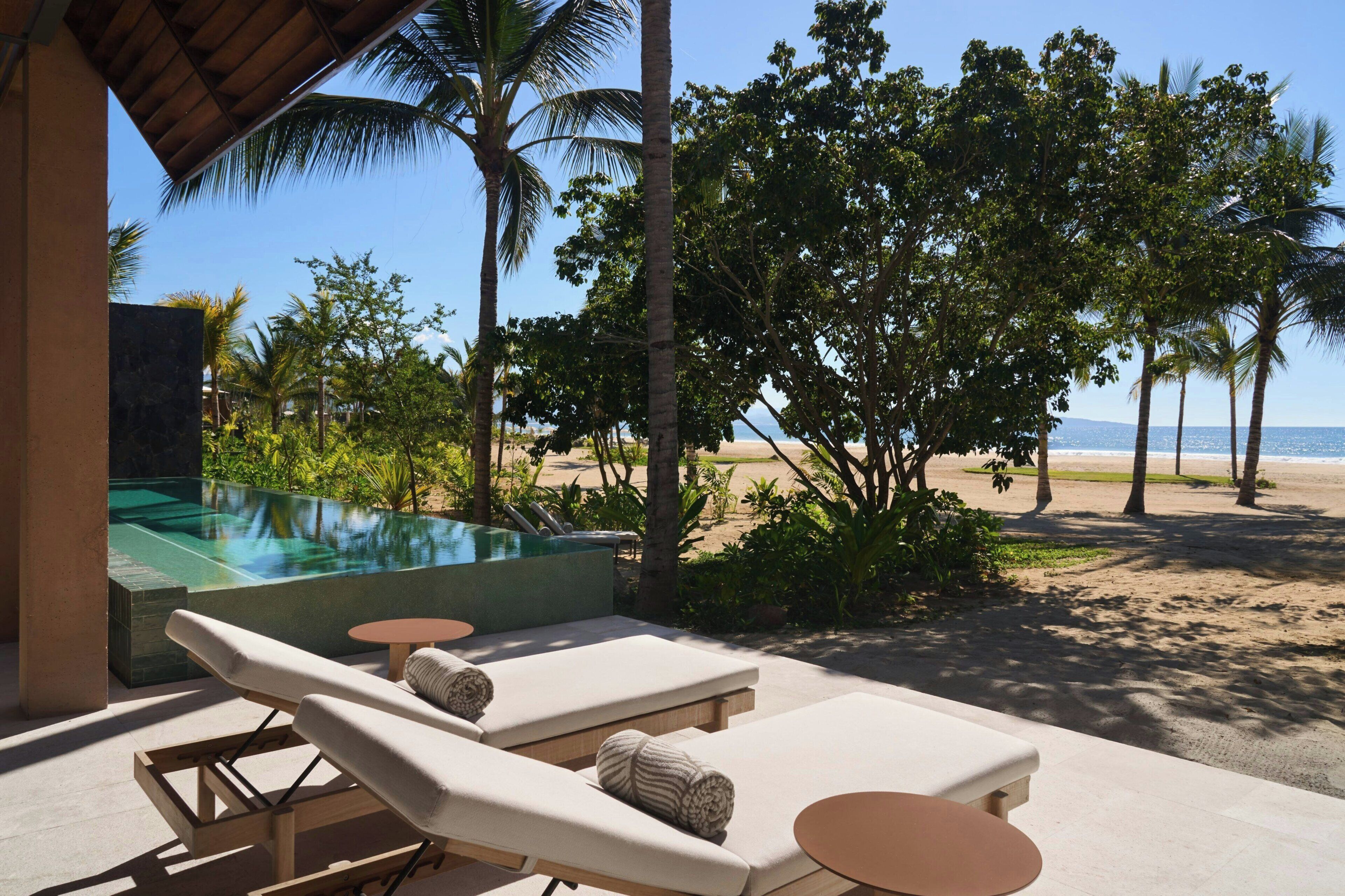 A poolside lounge with sun loungers, a small table, and a view of the beach and ocean.