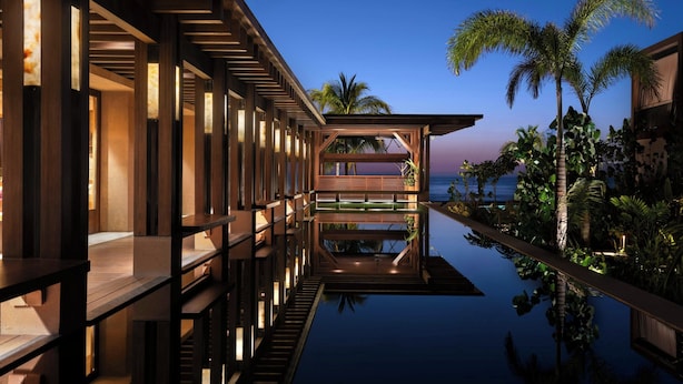 Um resort moderno com piscina infinita de fundo de vidro, deck de madeira e palmeiras.