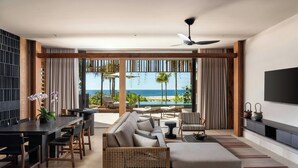 Uma sala de estar moderna com sofá, mesa de jantar, cadeiras, televisão de tela plana e vista para a praia.