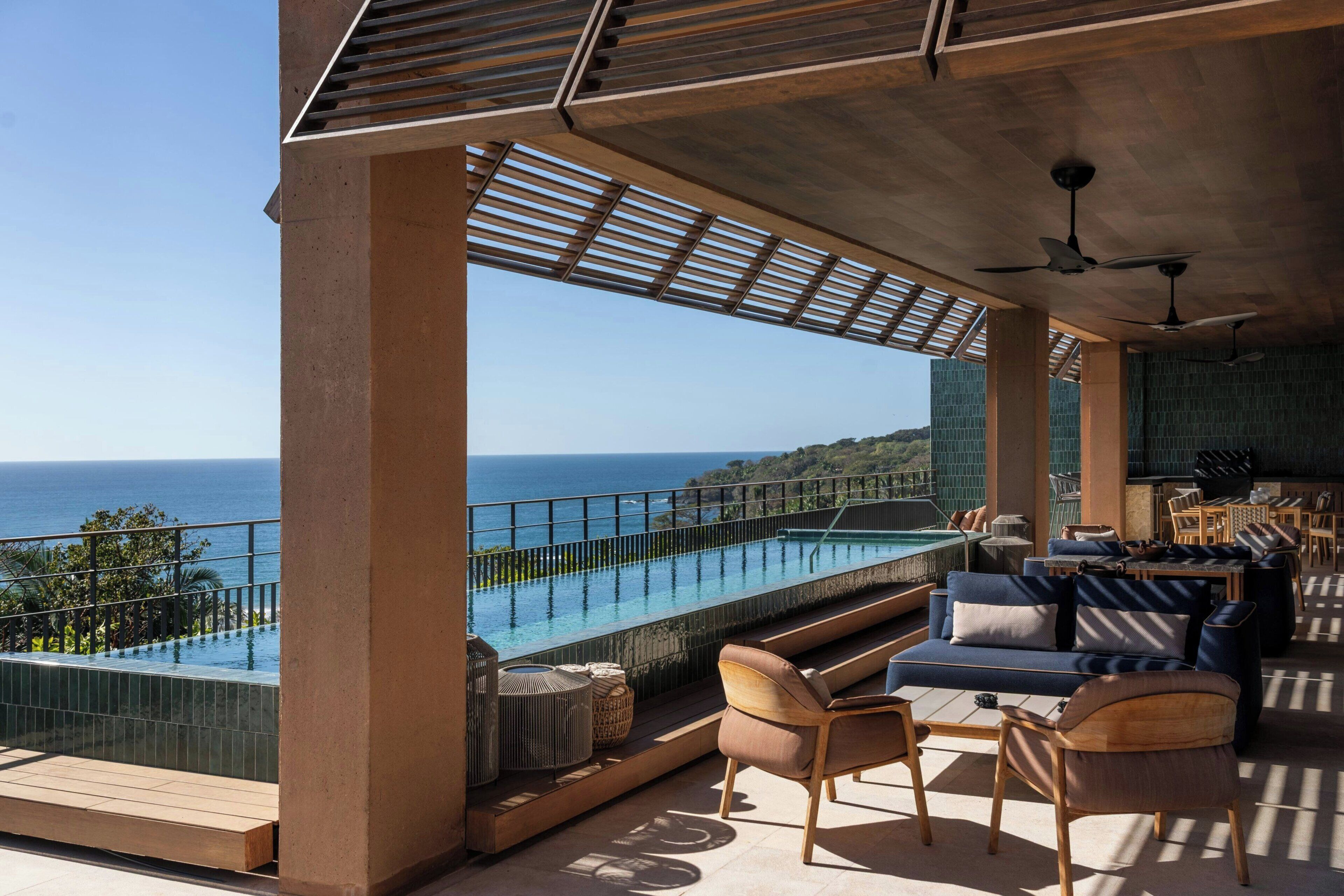 A modern outdoor lounge area with a pool, seating, and a view of the ocean.