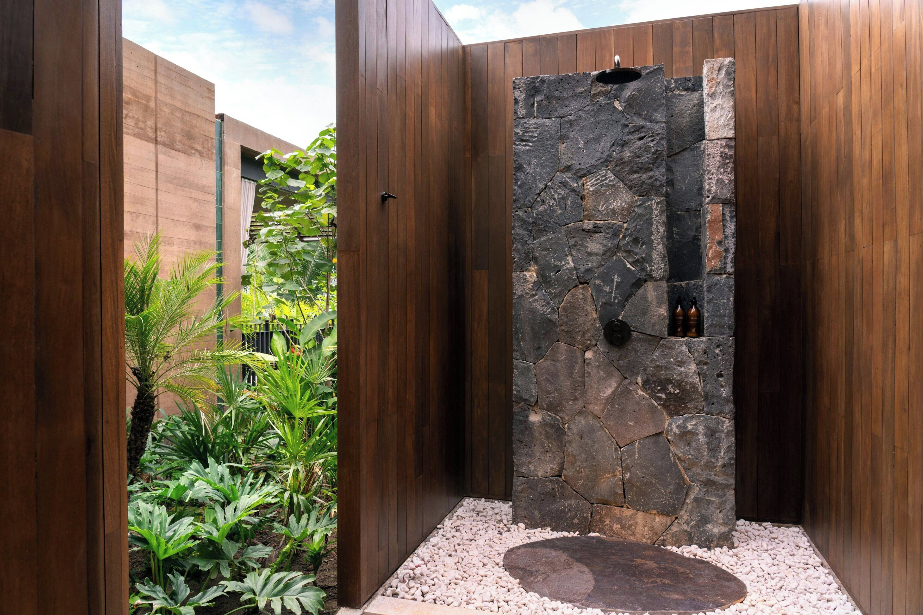 A modern shower enclosure with a stone wall and wooden paneling.
