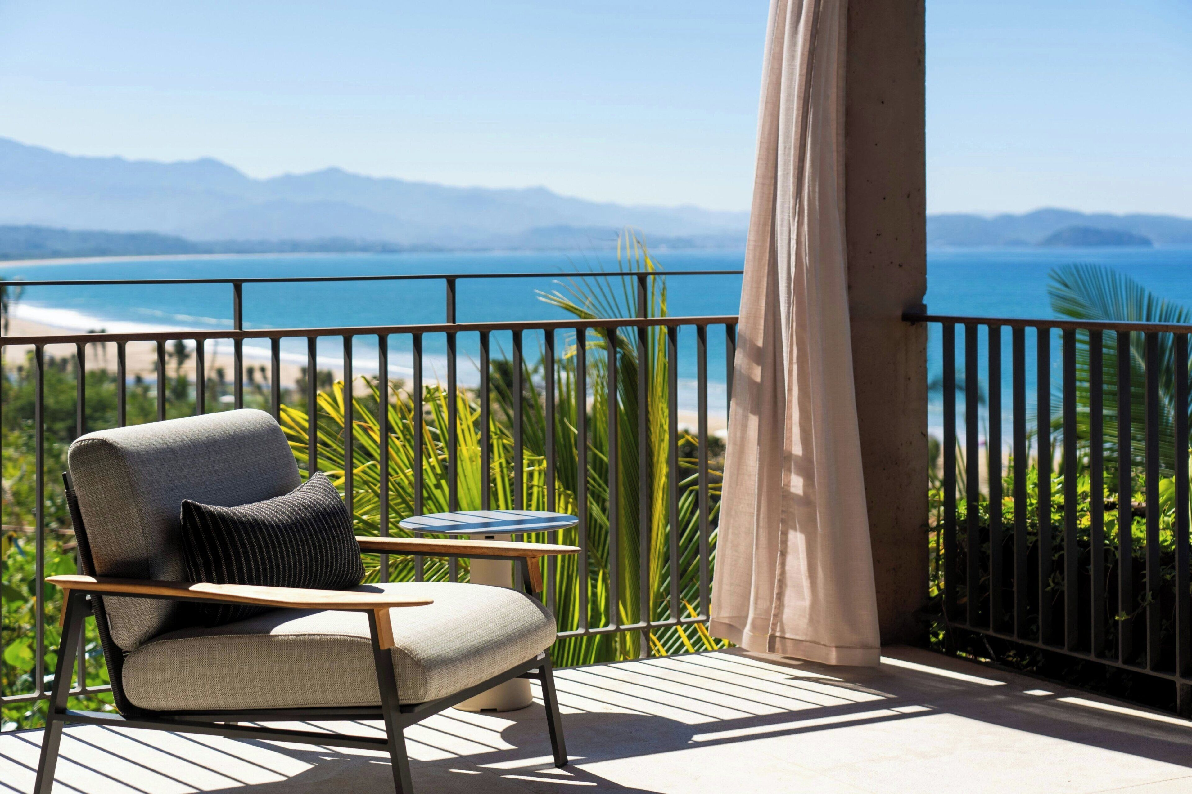 A balcony with a chair, a table, and a view of the sea and mountains.