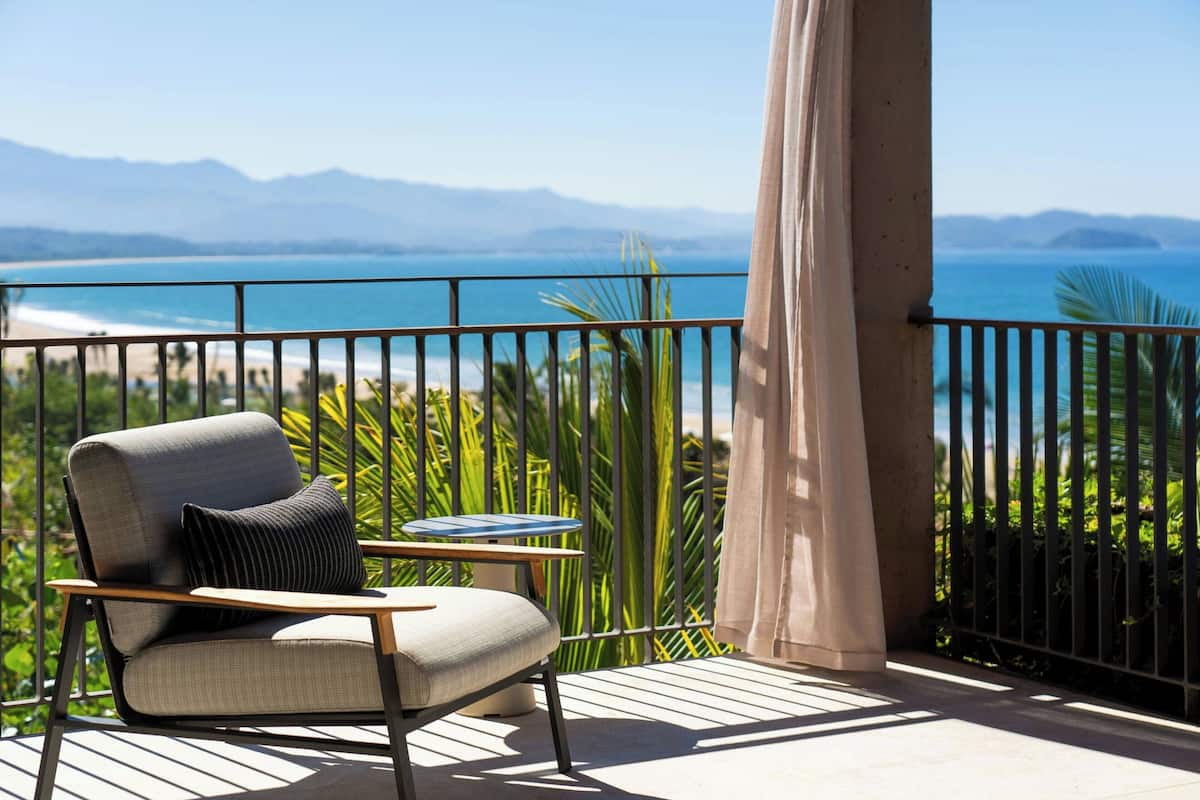A balcony with a chair, a table, and a view of the sea and mountains.