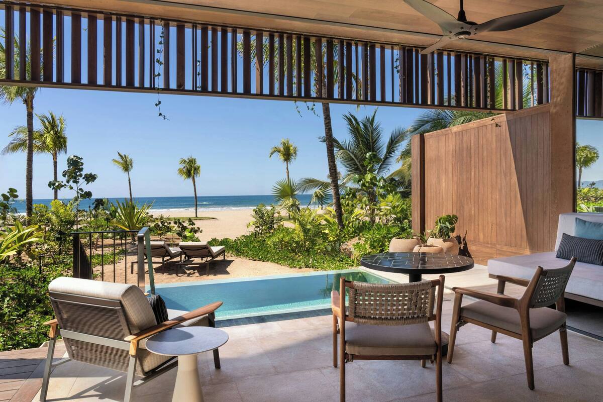 A poolside area with a view of the beach, outdoor furniture, and a ceiling fan.