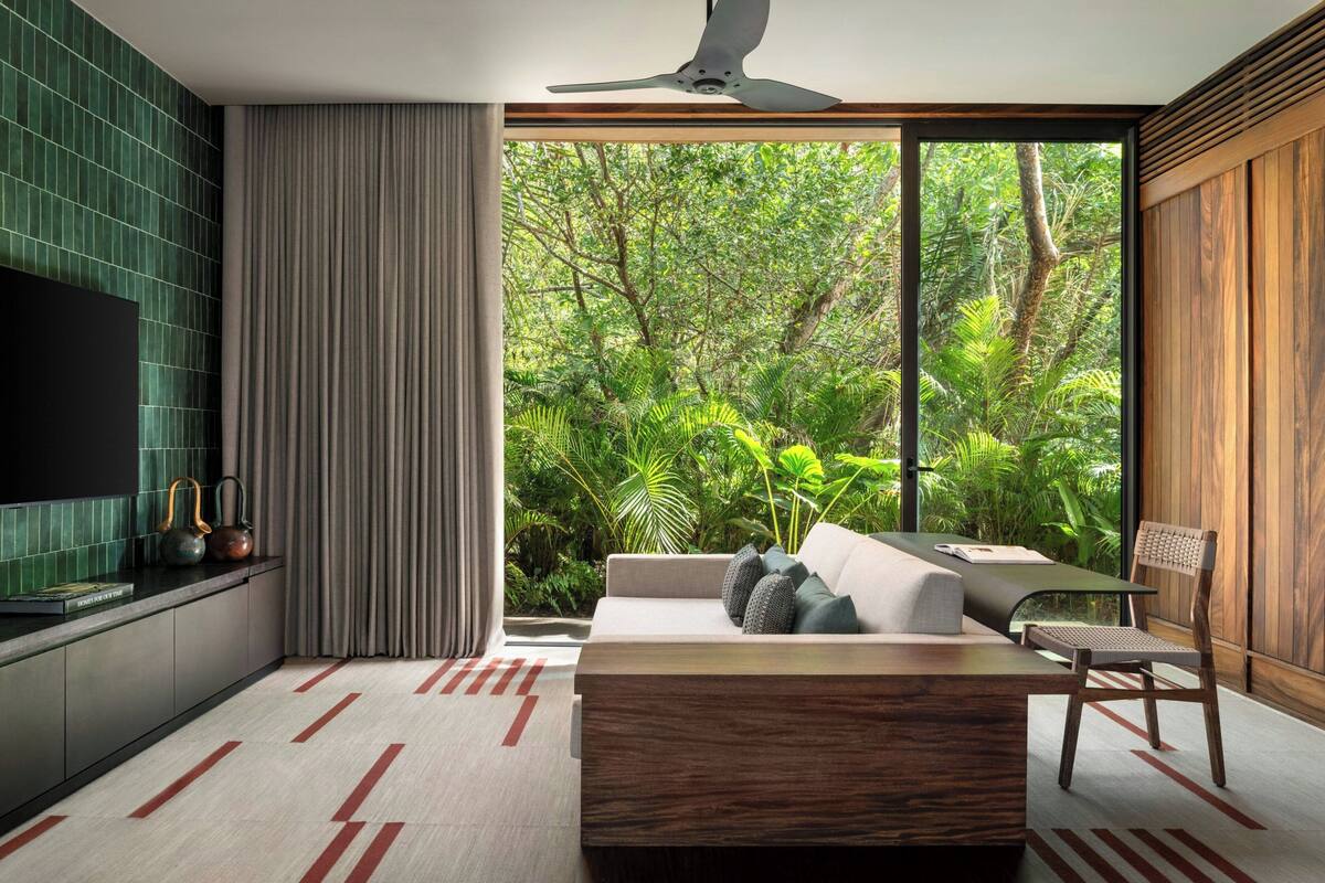 A modern living room with a large window, a sofa, a coffee table, and a television on a wall.