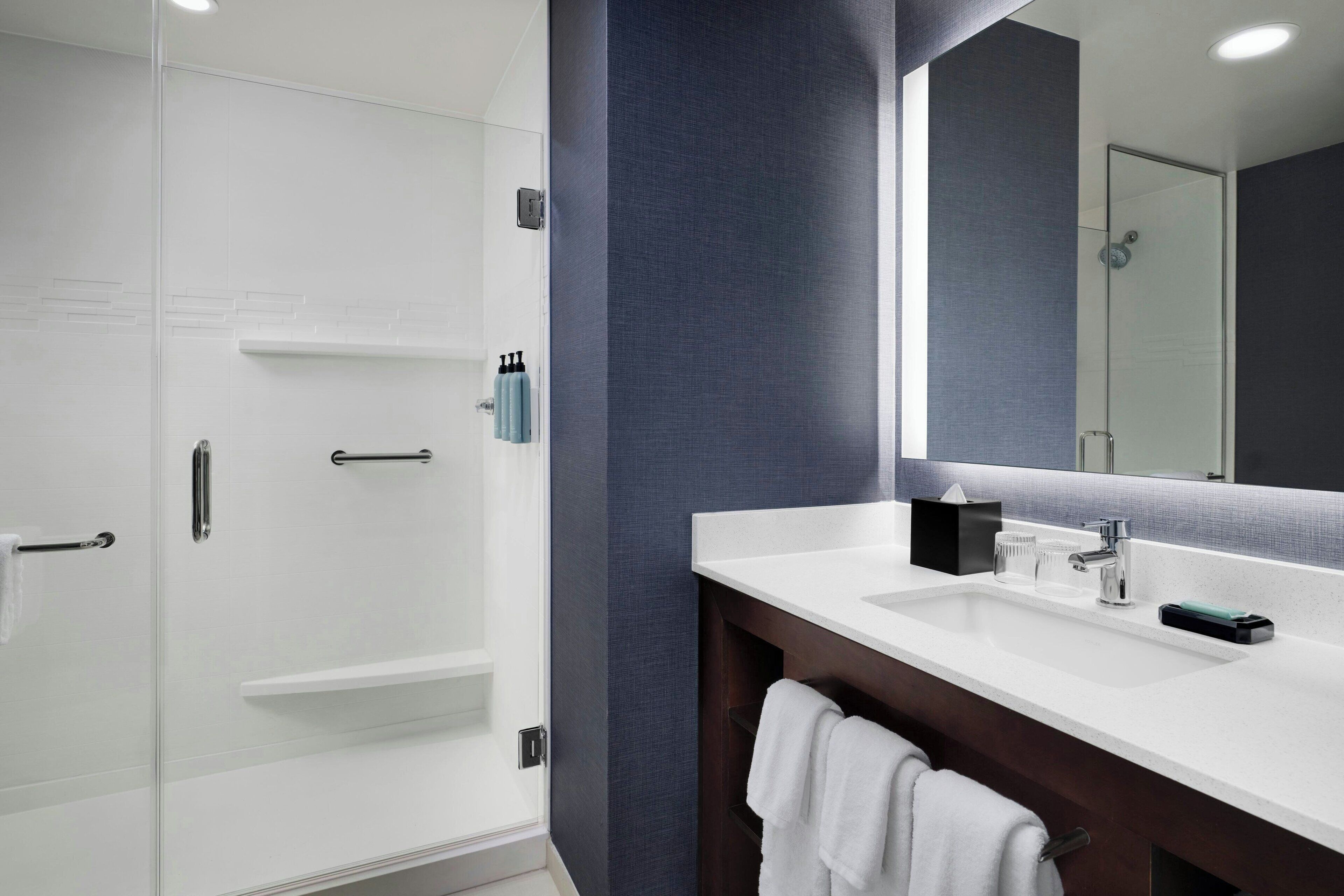 Une salle de bain moderne avec un meuble-lavabo blanc, un grand miroir et une cabine de douche en verre.