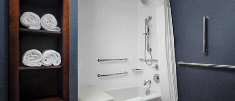 A modern bathroom with a bathtub, shower, and toilet. There are towels neatly rolled and placed in a wooden shelf.
