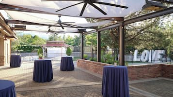 An outdoor patio area with brick flooring, covered by a canopy with ceiling fans, and tables with dark tablecloths.