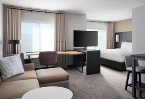 A hotel room with a bed, a desk with a TV, a sofa, and a small table.