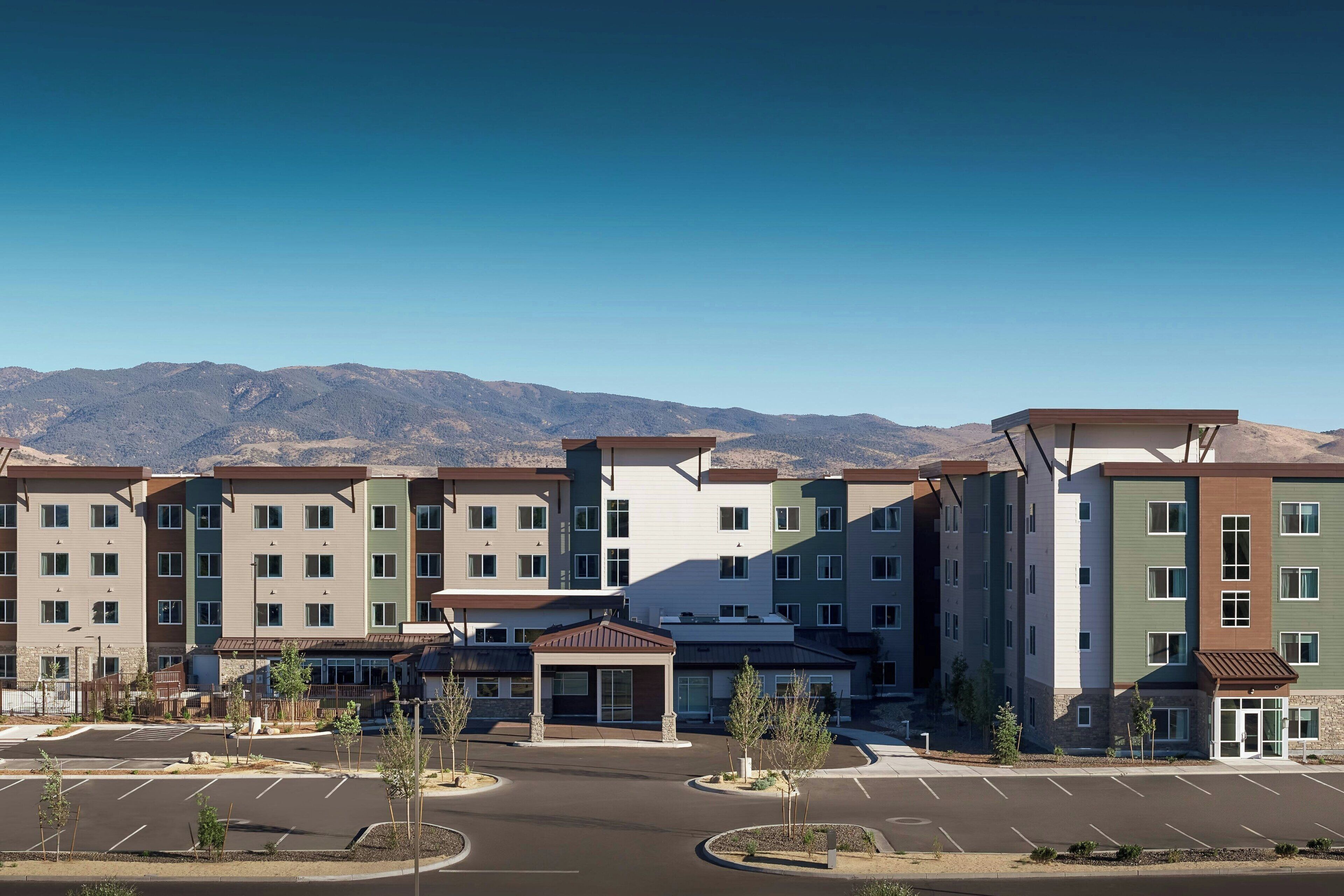 A multi-story residential building with a central courtyard, parking lot, and mountains in the background.