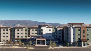 A multi-story residential building with a central courtyard, parking lot, and mountains in the background.
