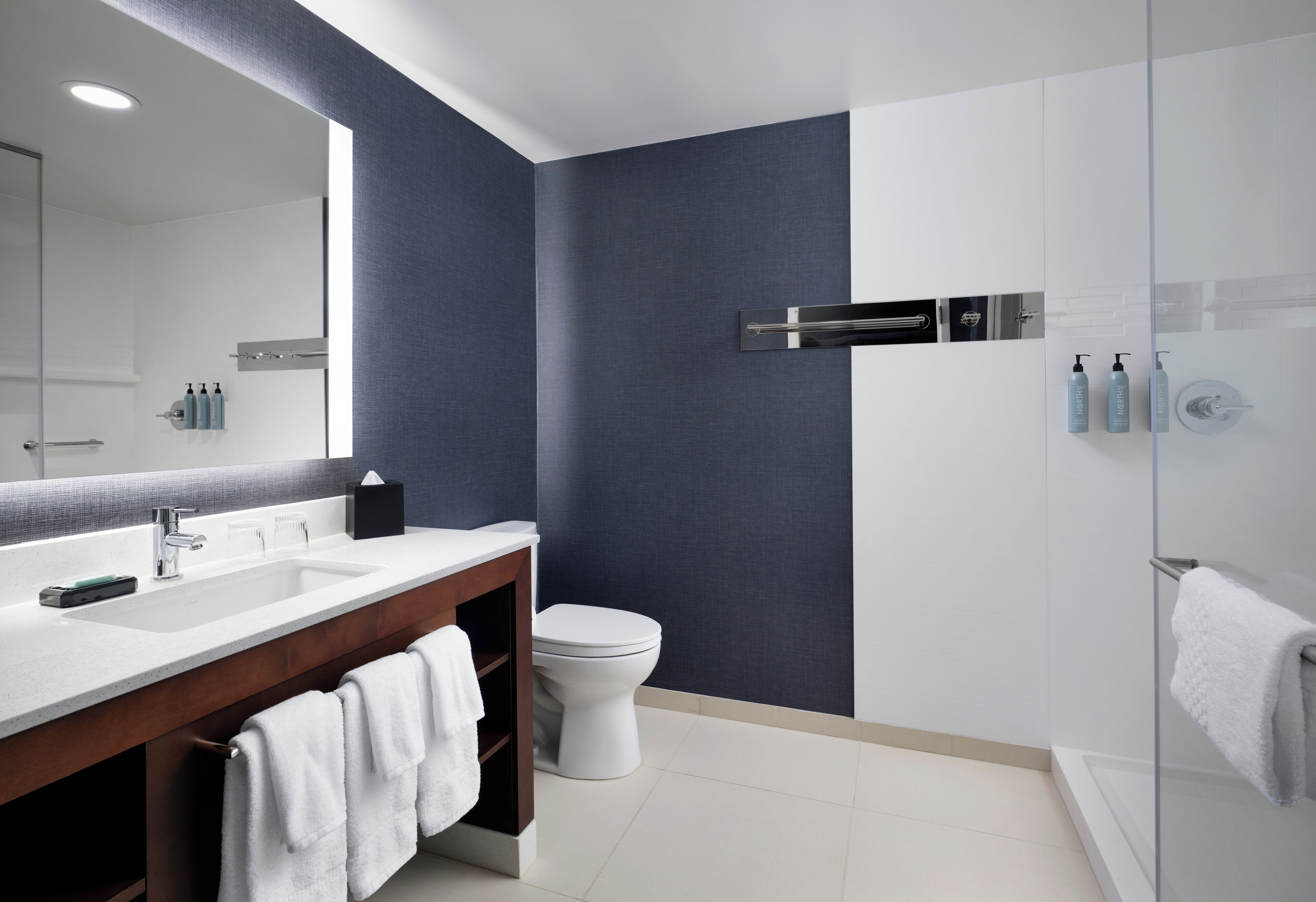A modern bathroom with a large mirror, dual sinks, a toilet, and a glass shower enclosure.