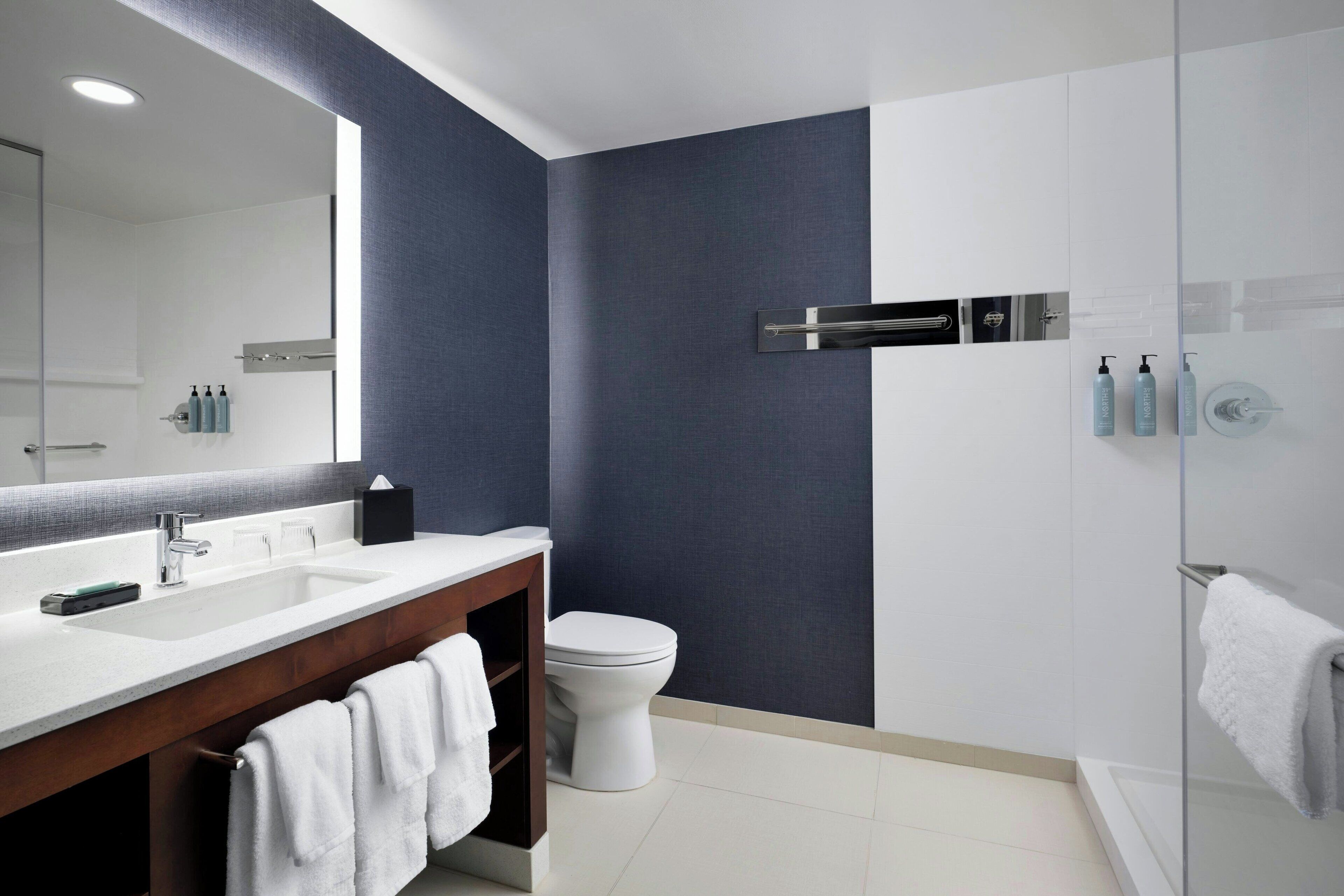 Une salle de bain moderne avec un grand miroir, deux lavabos, des toilettes et une douche à parois de verre.